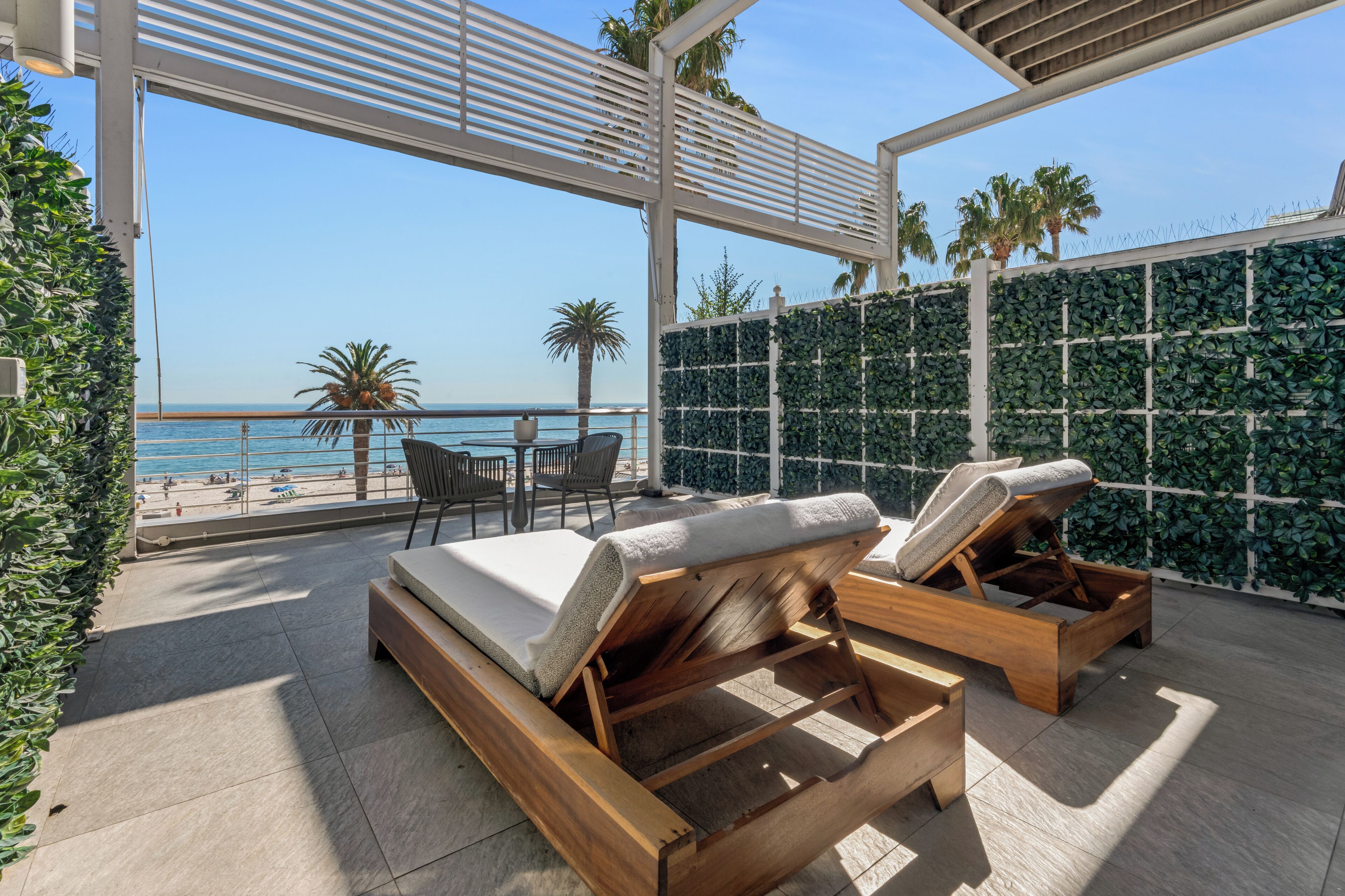 Un balcón con cama, sillones de descanso y vista a la playa.