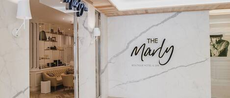 A hotel lobby with a marble wall and a sign reading "THE Mandy Boutique Hotel & Spa".