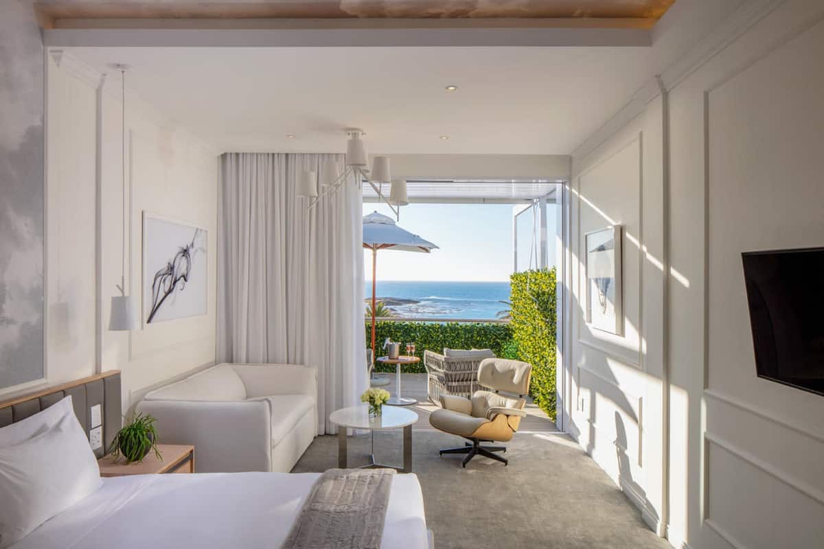 Une chambre d’hôtel moderne, équipée d’un lit, d’un canapé, d’une chaise, d’une petite table et offrant une vue sur l’océan.