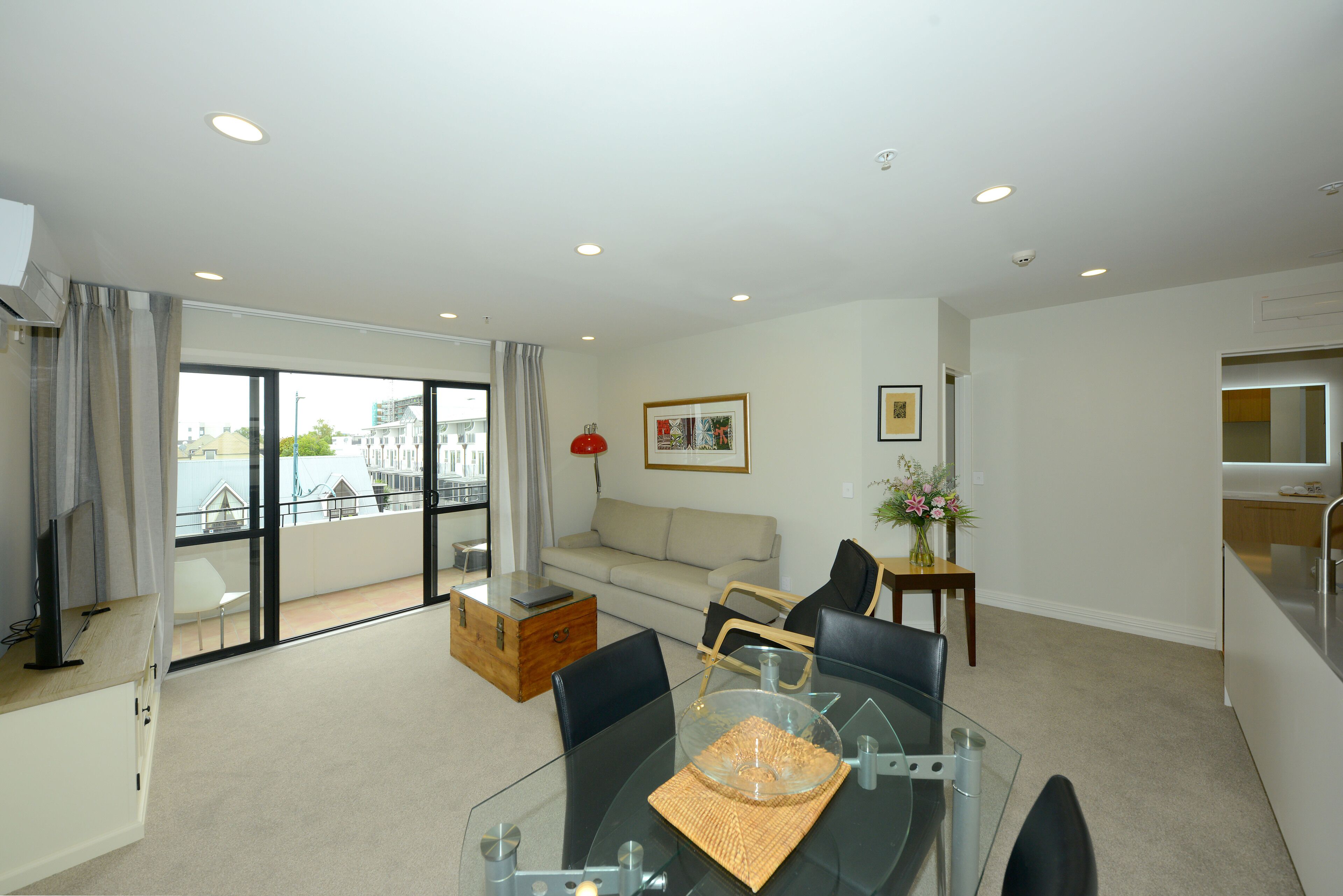 A modern living room with a glass dining table, a sofa, and a view of the city.