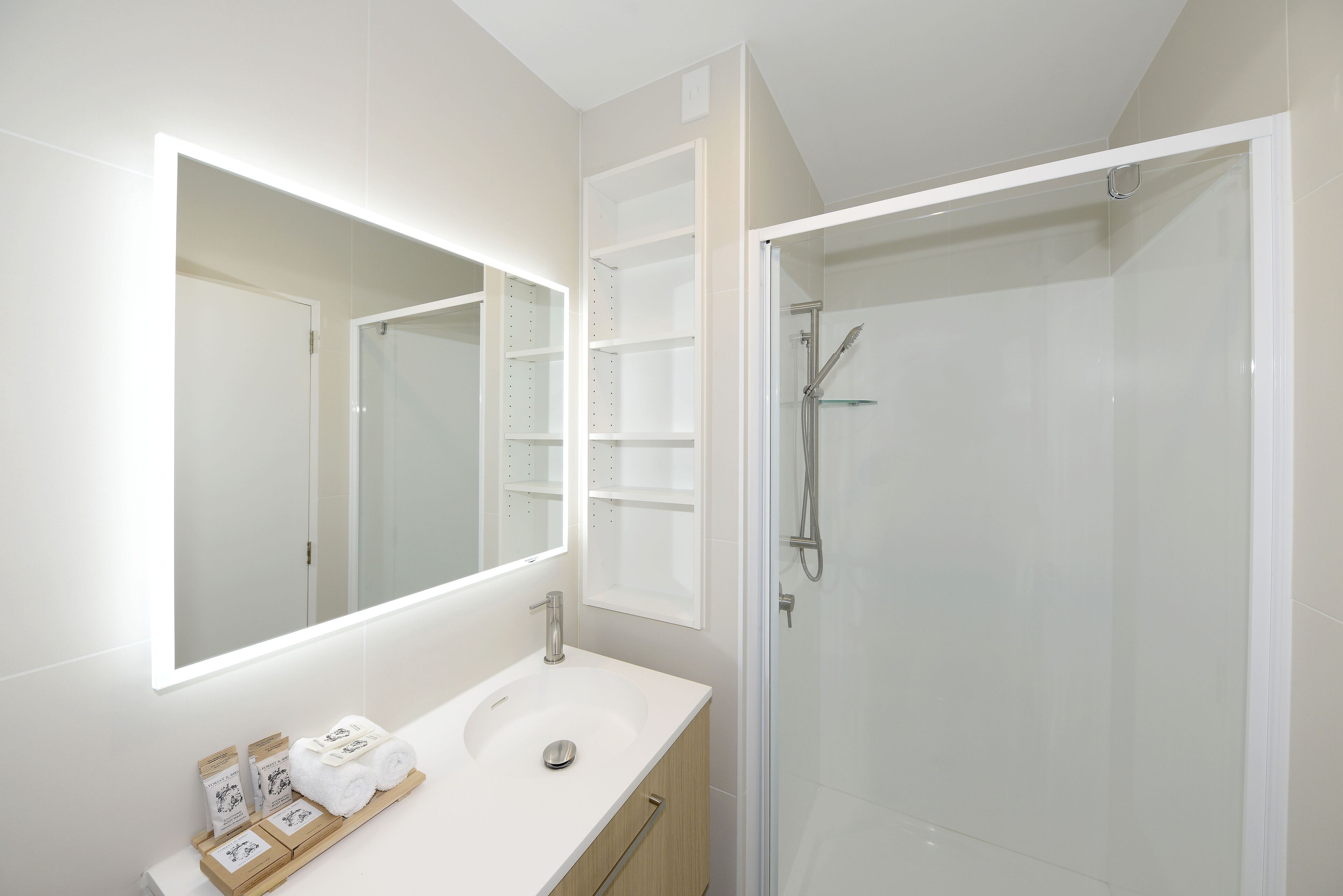 A modern bathroom with a large mirror, a white sink, and a glass-enclosed shower.