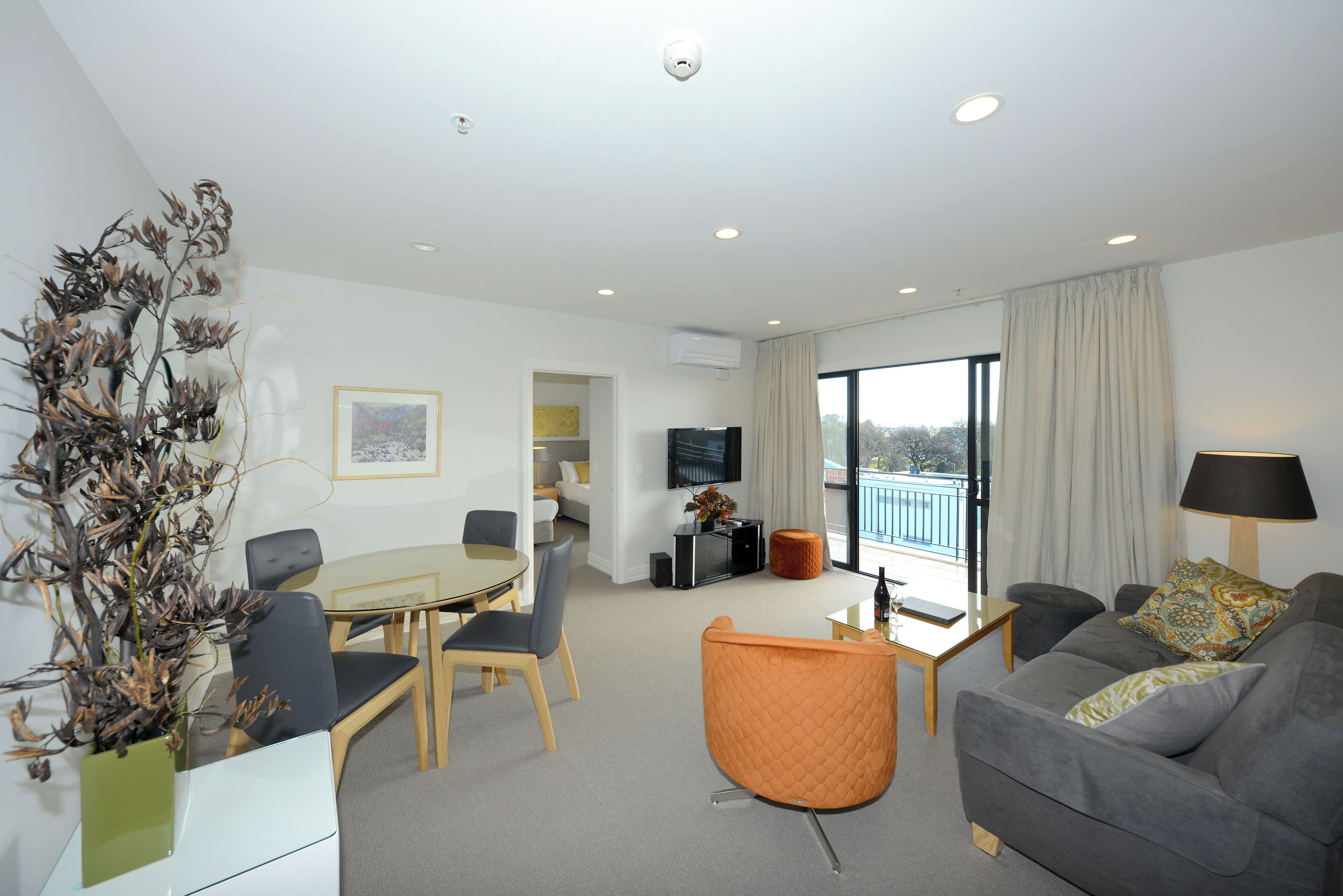Ein modernes Wohnzimmer mit Essbereich, einer Couch, einem Fernseher und Blick auf einen Balkon.