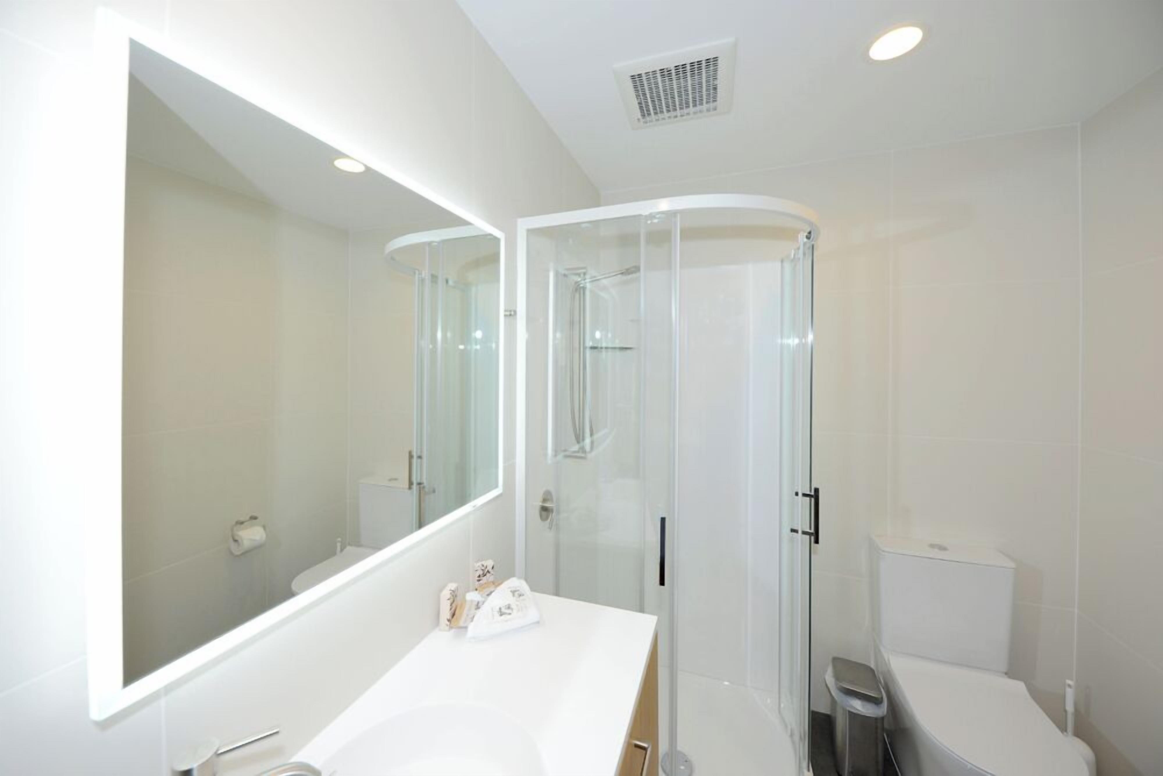 A modern bathroom with a glass-enclosed shower, a white vanity, and a large mirror.