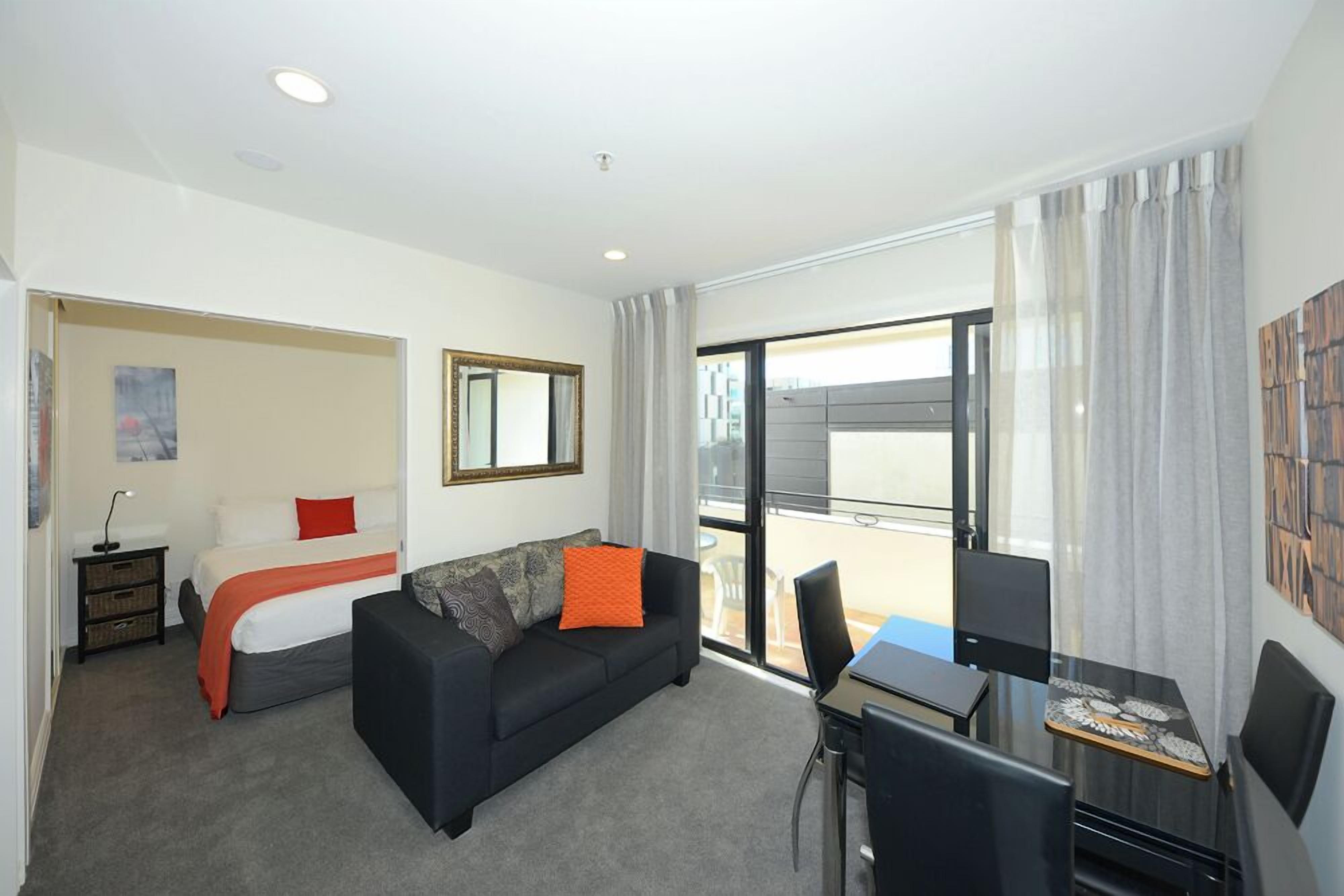 A modern hotel room with a bed, a sofa, a desk, and a large window.