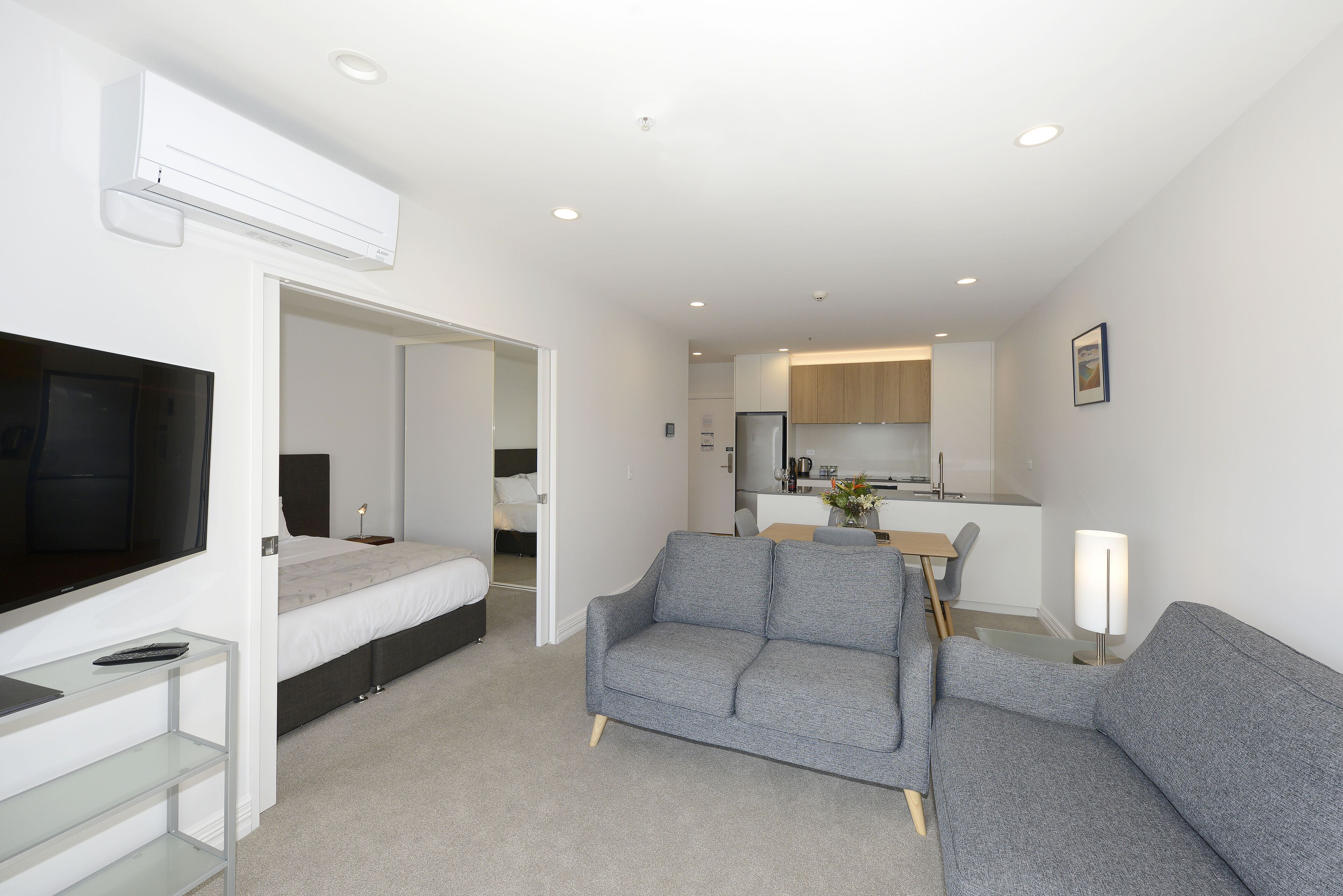 A modern living room with a grey sofa, a flat-screen TV, and a glass coffee table.