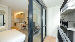 A modern hotel room with a bed, a desk, and a kitchenette. There is a balcony with a railing. - West Fitzroy Apartments (Christchurch)