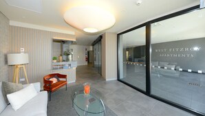 A modern living room with a sofa, a glass coffee table, and a lamp. There is a glass wall with the text "WEST FITZROY APARTMENTS" visible. - West Fitzroy Apartments (Christchurch)
