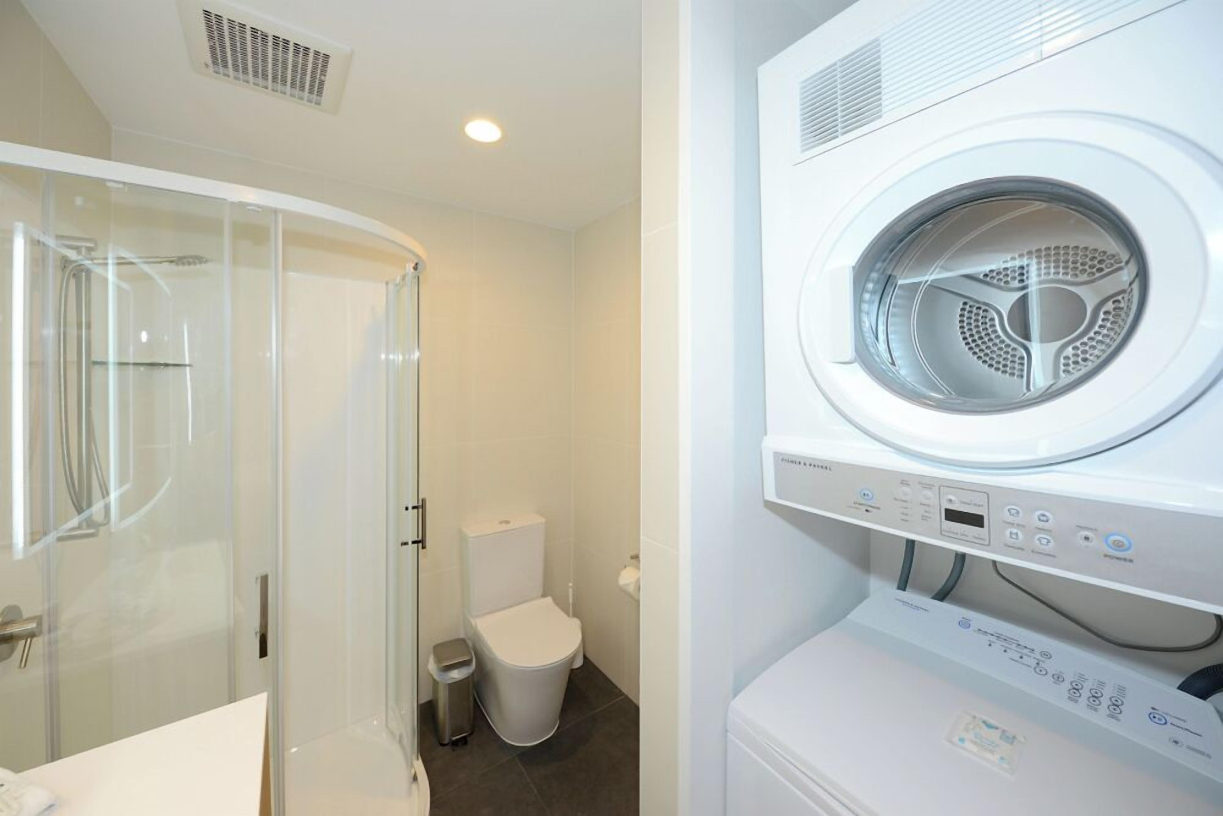 A modern bathroom with a glass-enclosed shower, a toilet, and a front-loading washing machine.