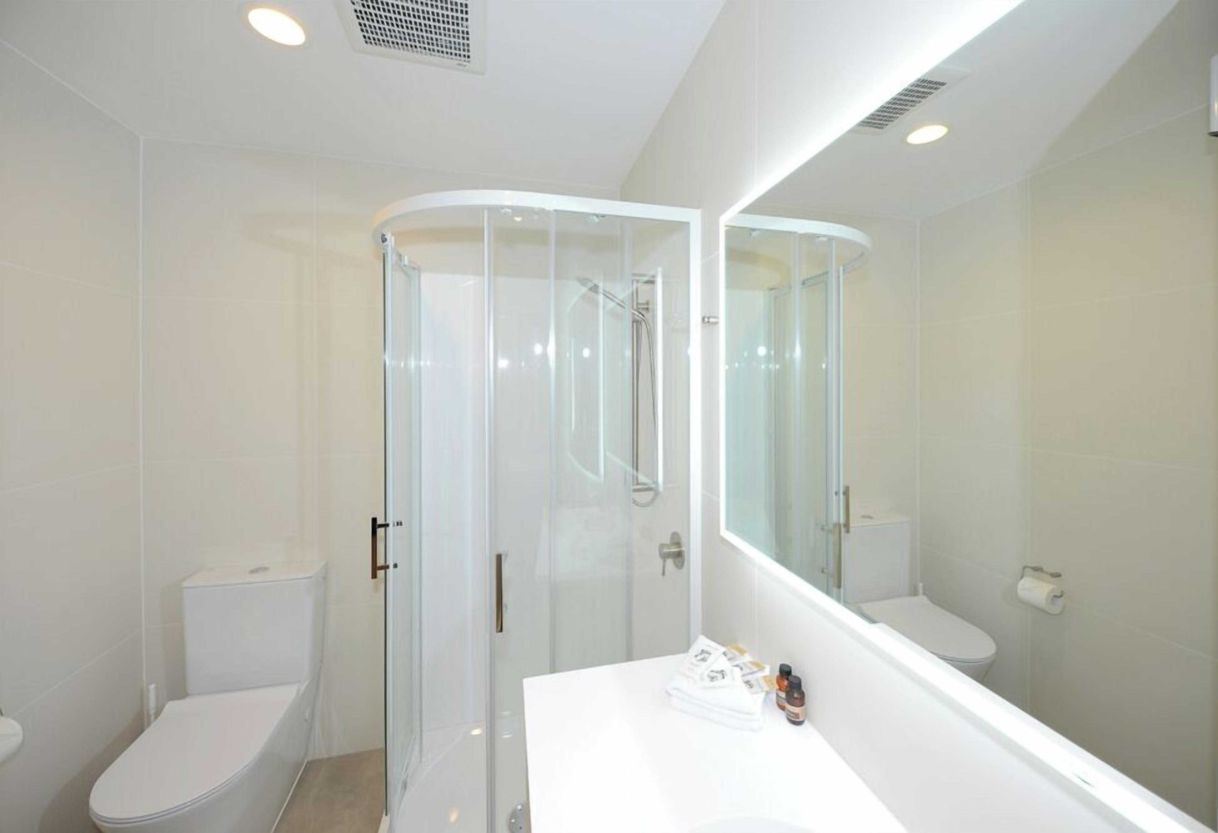 A modern bathroom with a glass-enclosed shower, a white sink, and a large mirror.