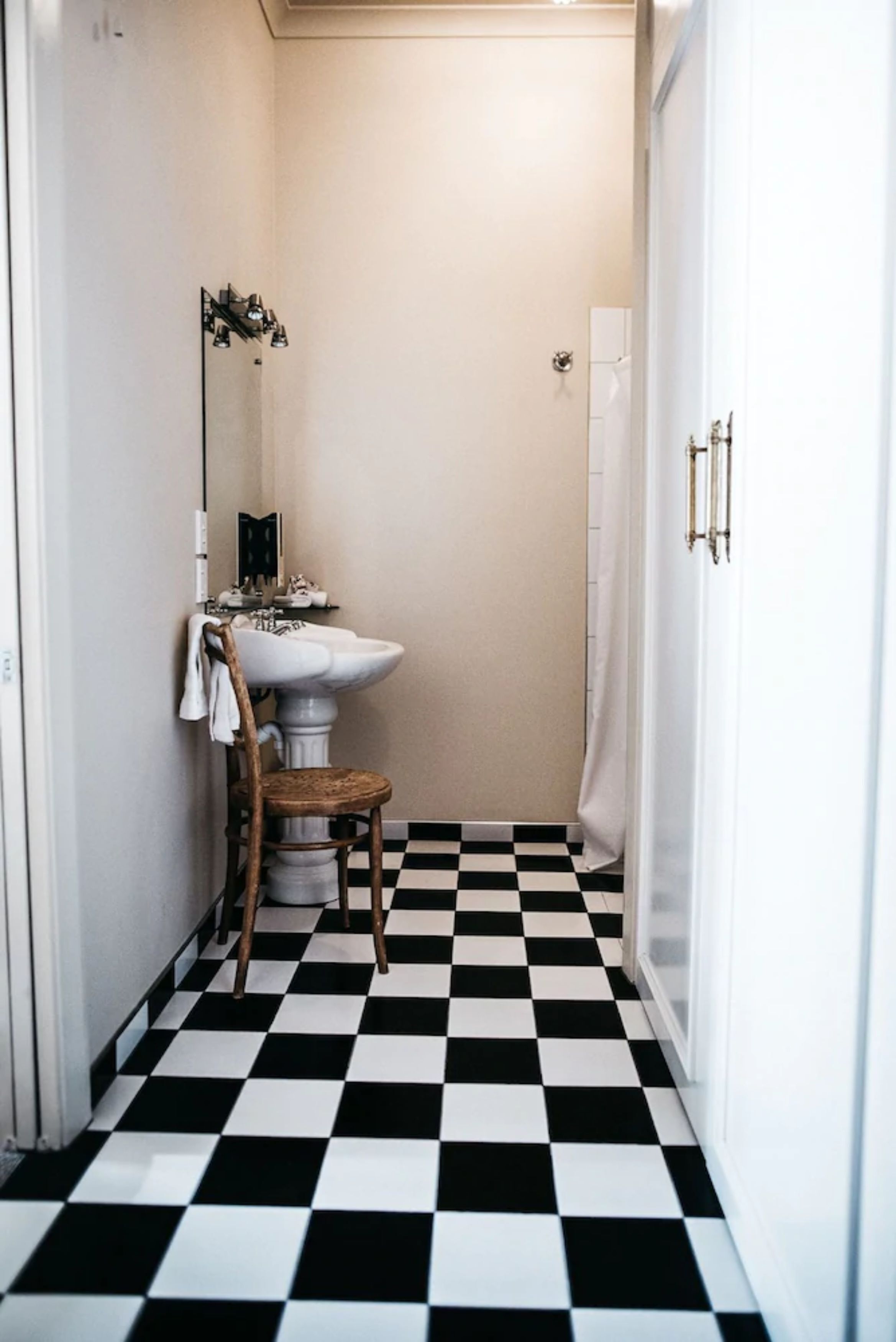 A bathroom with a white sink, a wooden chair, and a black and white checkered floor.