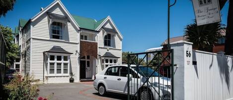 A white two-story building with a green roof, a gated entrance, and a sign for 'The Grange Boutique B&B and Hotel'.