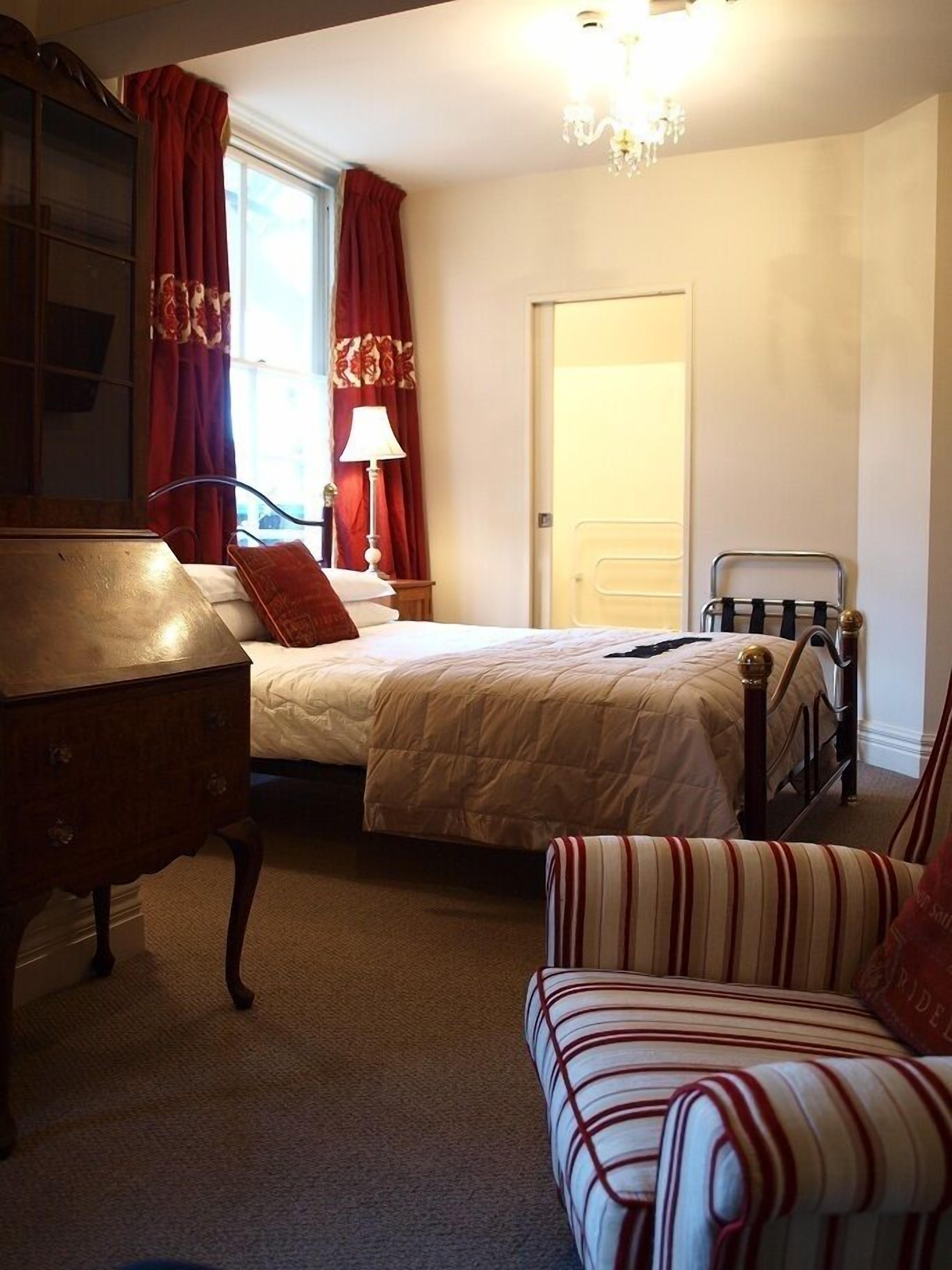 A bedroom with a bed, a chair, a nightstand, a lamp, and a wardrobe.