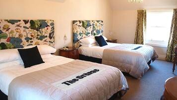 Ein Hotelzimmer mit zwei Betten, blumengemusterten Kopfteilen, einem Kronleuchter und einem Fenster mit Vorhängen.