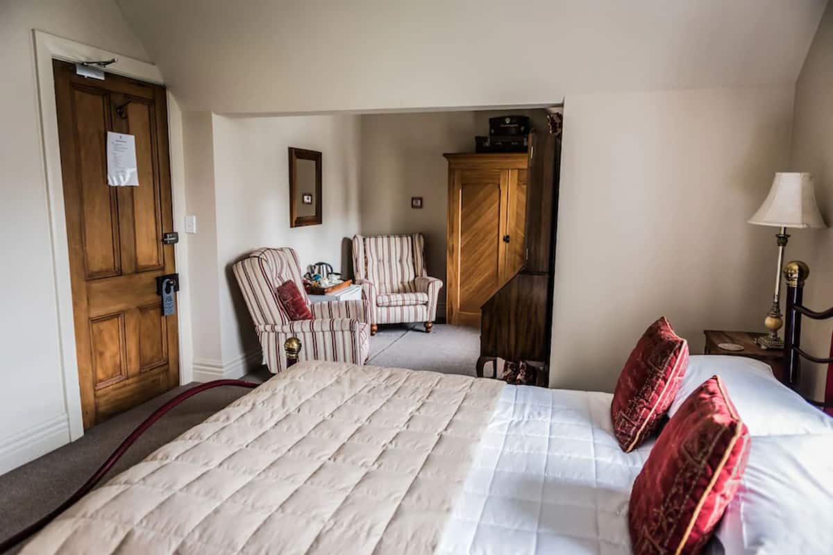 Una habitación de hotel con una cama grande, dos sillones, un aparador de madera y una lámpara.