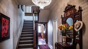 Una gran escalera con un candelabro, un escritorio de madera con un espejo y una obra de arte enmarcadas en rojo en la pared.