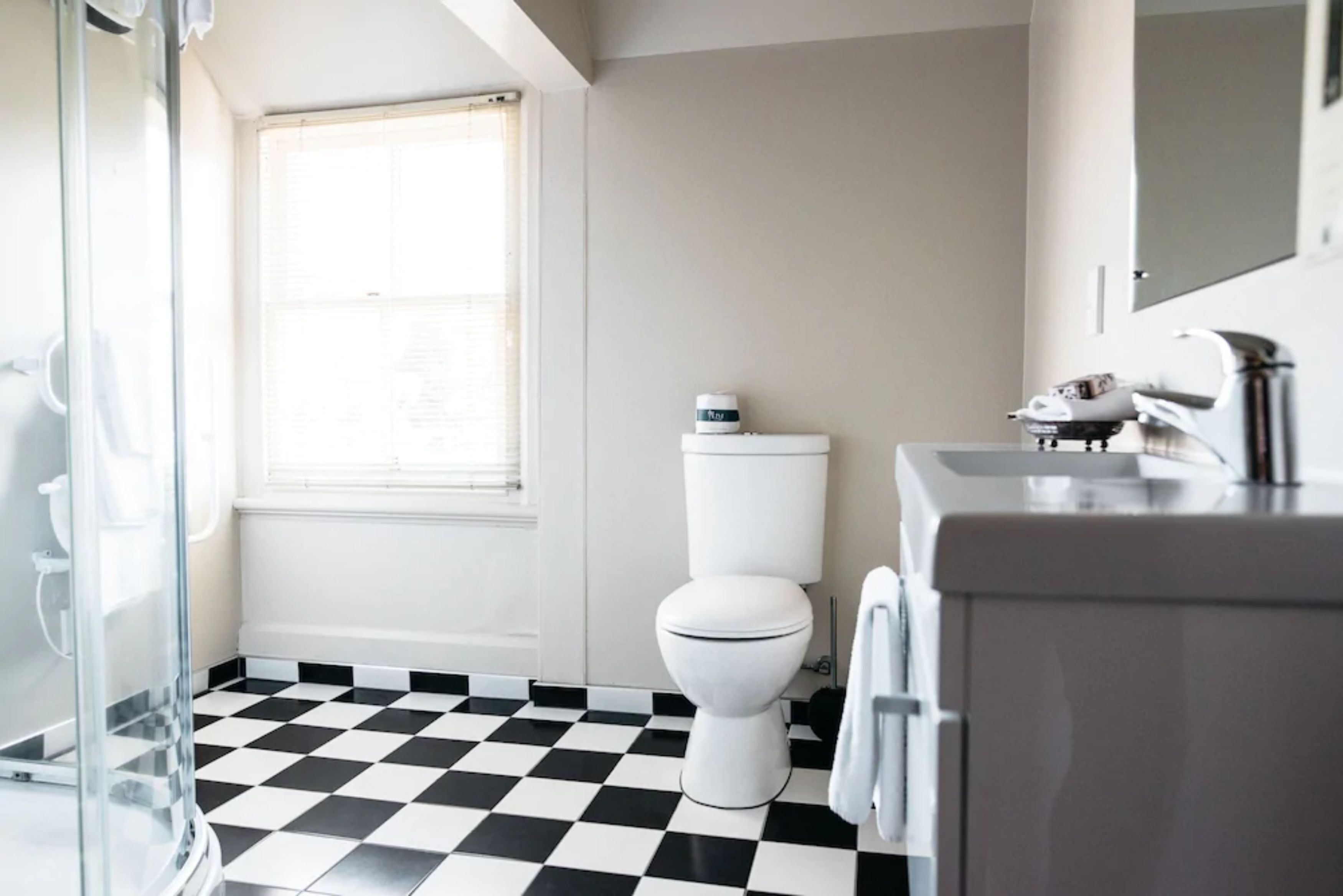 A bathroom with a black and white checkered floor, a toilet, a glass shower enclosure, and a sink with a mirror.