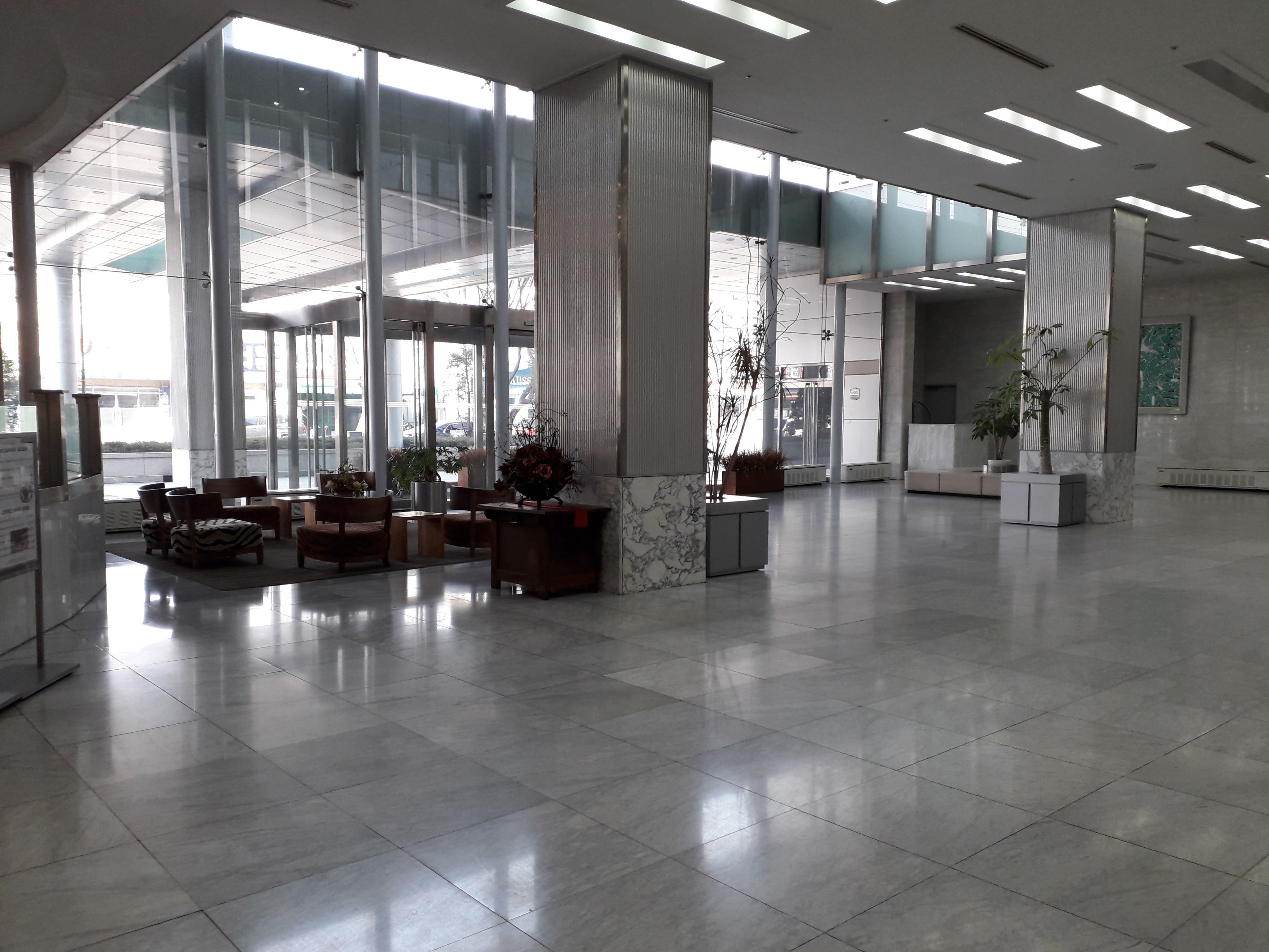 A spacious lobby with large windows, a seating area with chairs and tables, and potted plants.