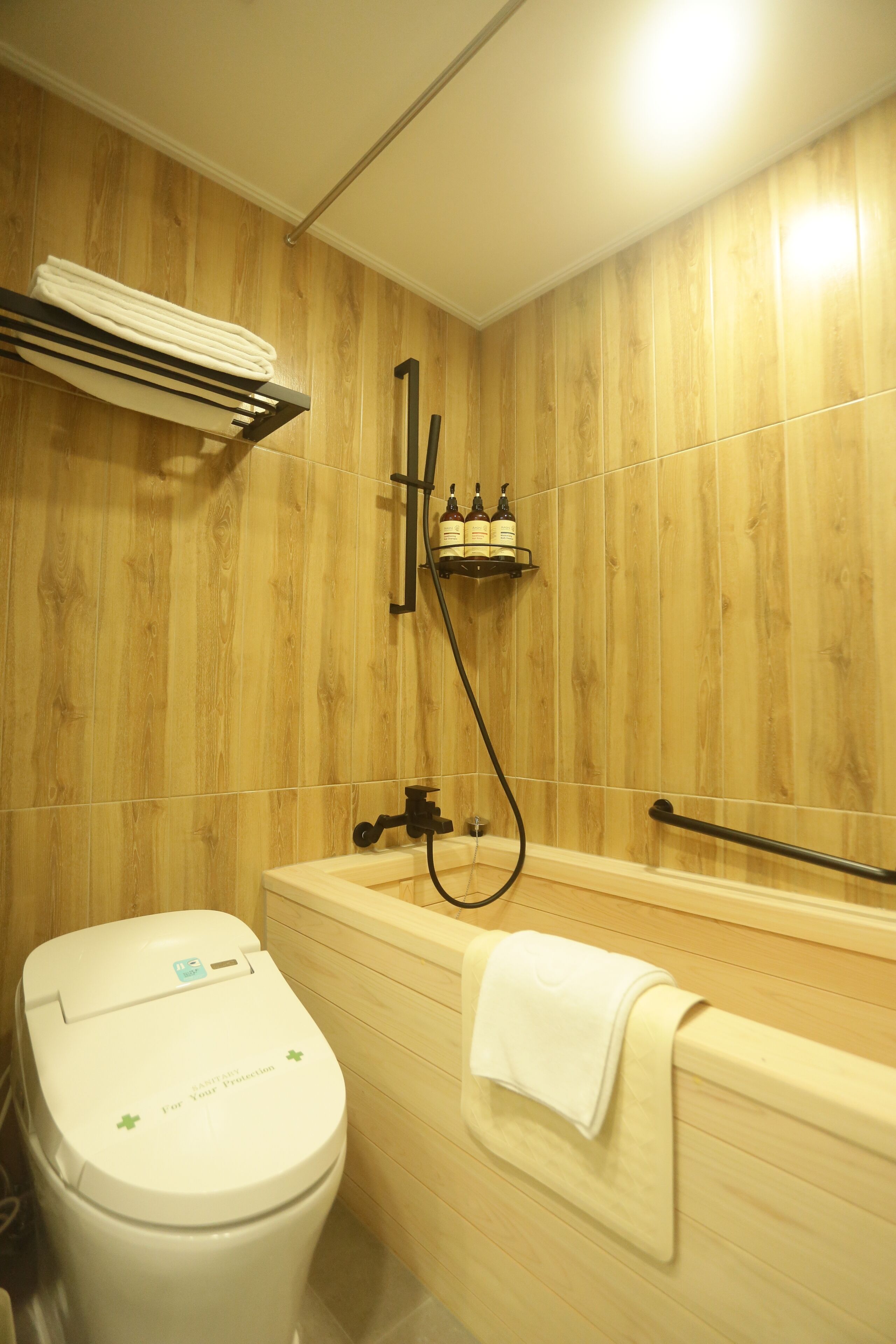 A bathroom with a wooden wall, a white toilet, a bathtub, and a towel rack.