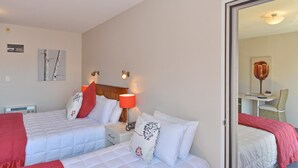 A hotel room with two beds, a bedside table with a lamp, a chair, and a desk with a chair. - Addington Court Motel (Christchurch)