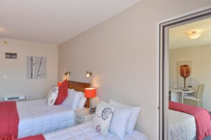 Hotellihuone, jossa on kaksi sänkyä, yöpöytä lampun kanssa, tuoli ja työpöytä tuolilla.