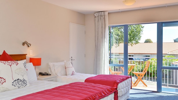 A hotel room with a bed, a nightstand, a lamp, a window, and a balcony with chairs. - Addington Court Motel (Christchurch)