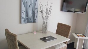 A hotel room with a dining table, two wicker chairs, a vase with branches, a flat-screen TV, and a small side table with a magazine. - Addington Court Motel (Christchurch)