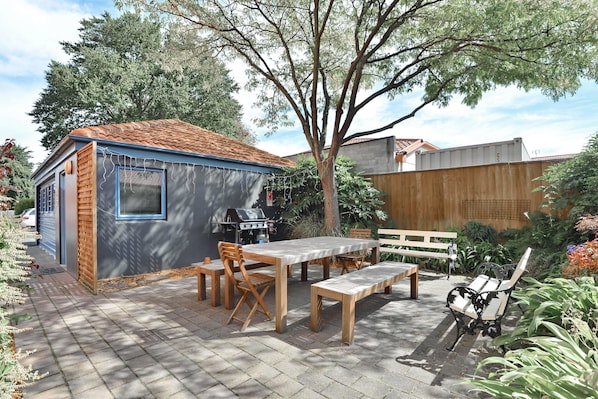 A backyard with a barbecue area, wooden table and chairs, and a bench.