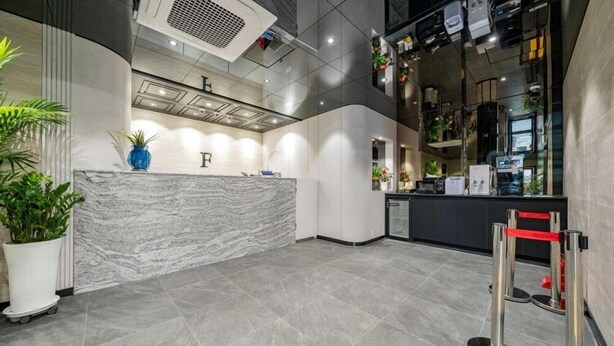 Una moderna zona de recepción con mostrador de mármol, plantas en macetas y una cocina visible al fondo.