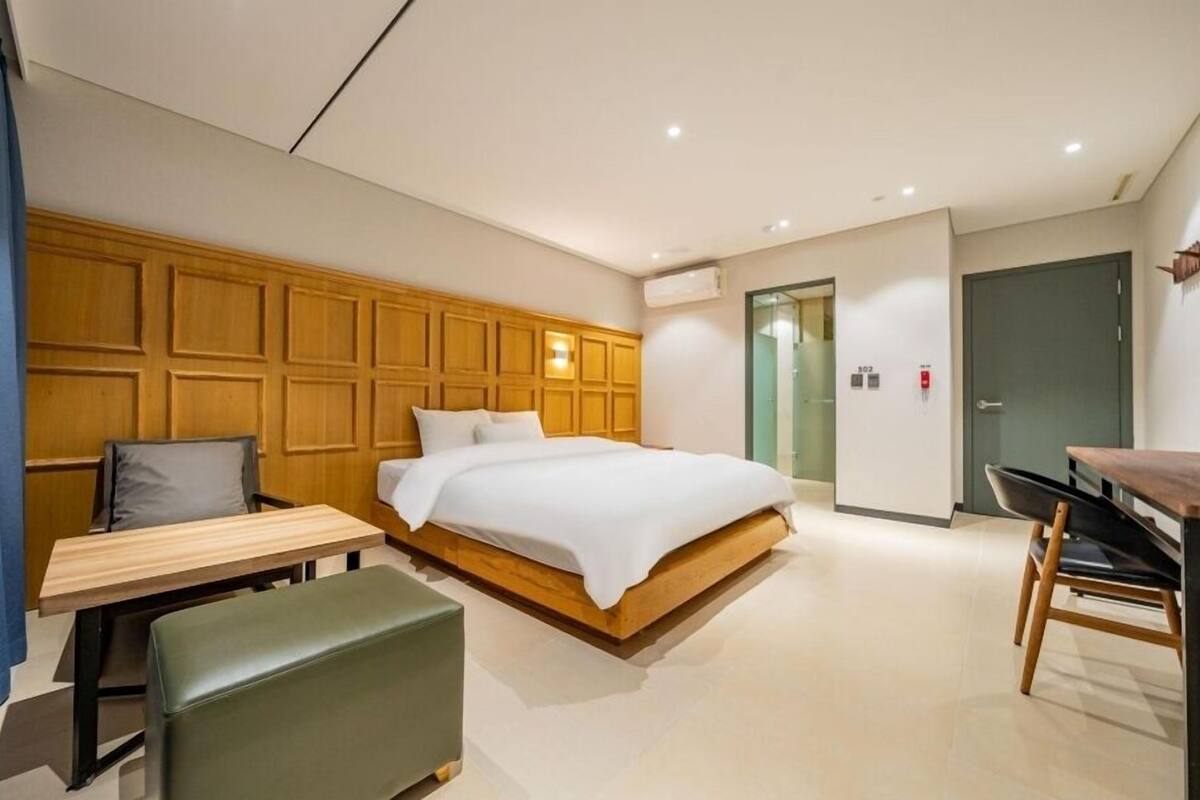 Une chambre d’hôtel moderne avec une tête de lit en bois, un lit simple, un bureau, une chaise et un banc.