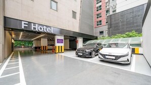 Entrada de un hotel con zona de estacionamiento para coches, un cartel que indica F Hotel y un edificio de diseño moderno.