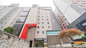 Entrada de hotel con fachada moderna, un arco rojo destacado y un letrero que indica que es el F Hotel.