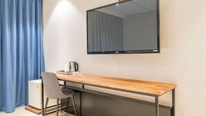 Una habitación moderna con un escritorio de madera, una silla, un televisor de pantalla plana en la pared y un pequeño calentador en el suelo.