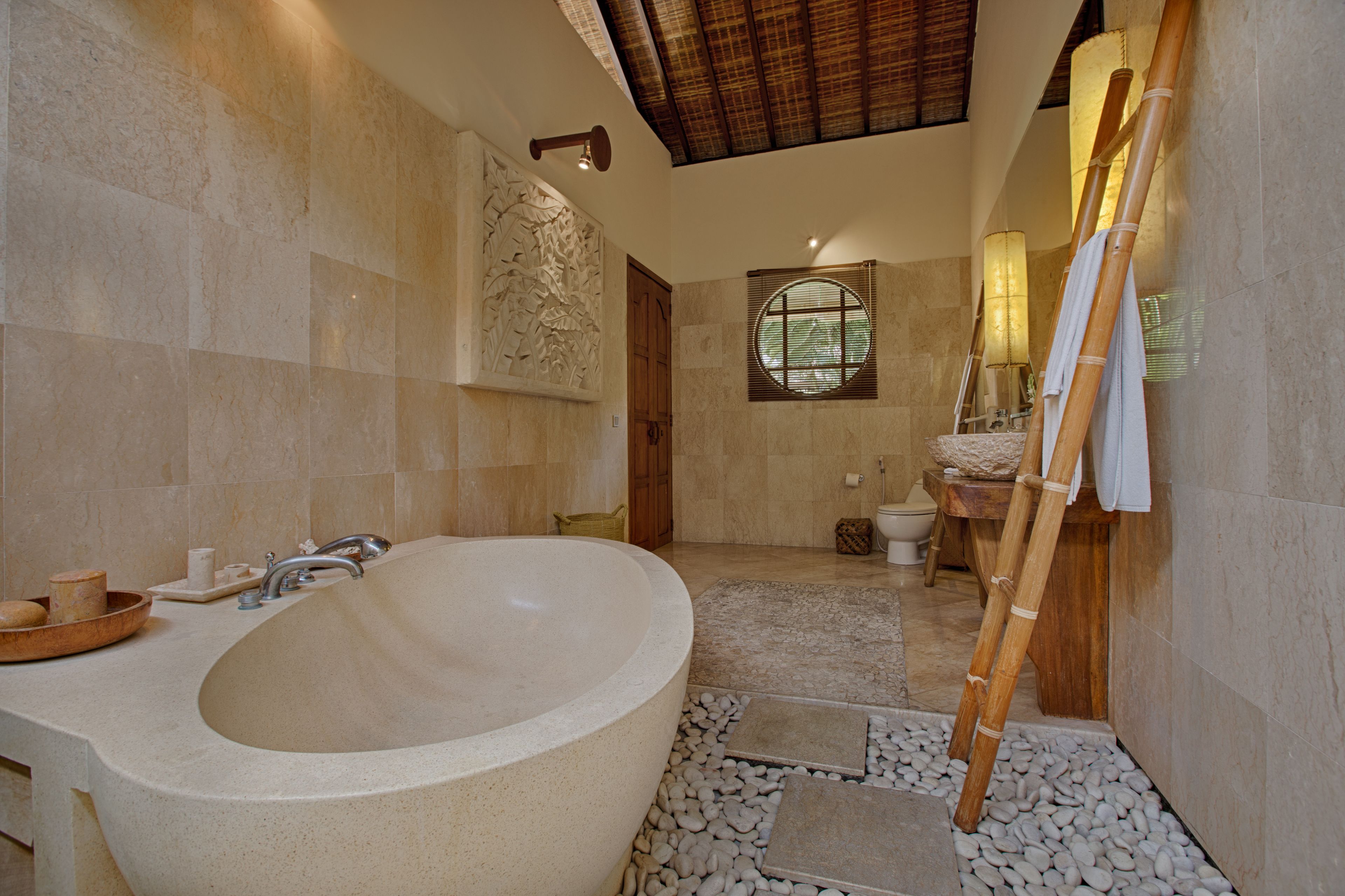 A bathroom with a large bathtub, a wooden ladder, and a stone floor.