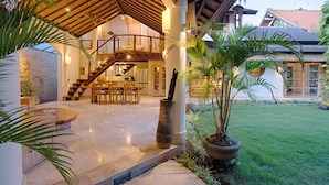 A spacious outdoor area with a stone wall, a wooden staircase, and a dining area with chairs and tables. - Mayana Villas (Canggu)