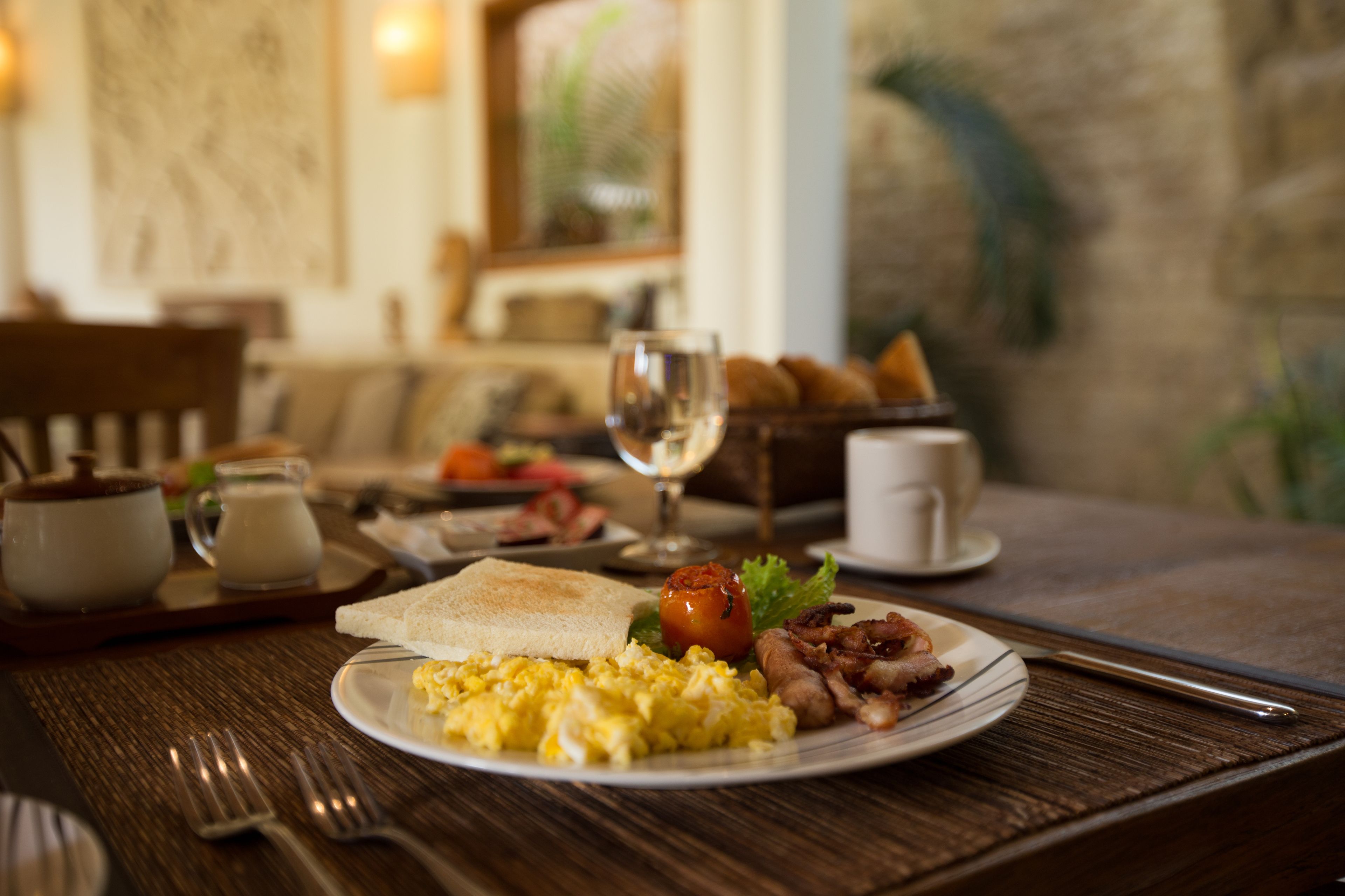 A breakfast setting with toast, scrambled eggs, bacon, and a glass of water on a wooden table.