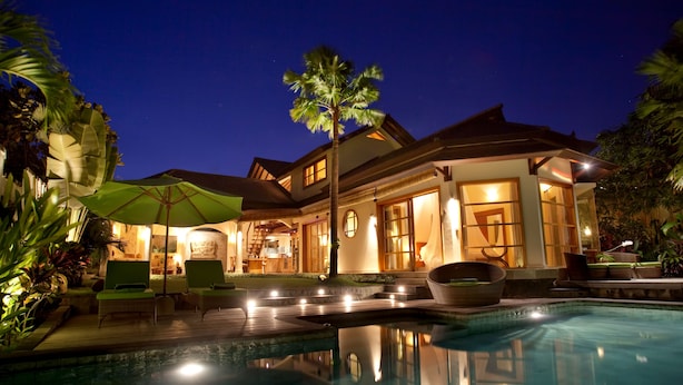 A well-lit resort with a swimming pool, lounge chairs, and a large umbrella. - Mayana Villas (Canggu)