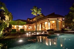 A well-lit resort with a swimming pool, lounge chairs, and a large umbrella. - Mayana Villas (Canggu)