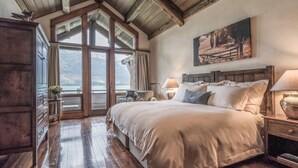 A bedroom with a large bed, wooden beams, a view of mountains, and a painting on the wall. - Blanket Bay (Glenorchy)