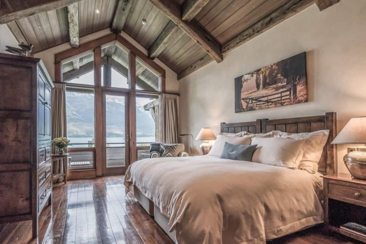 A bedroom with a large bed, wooden beams, a view of mountains, and a painting on the wall.