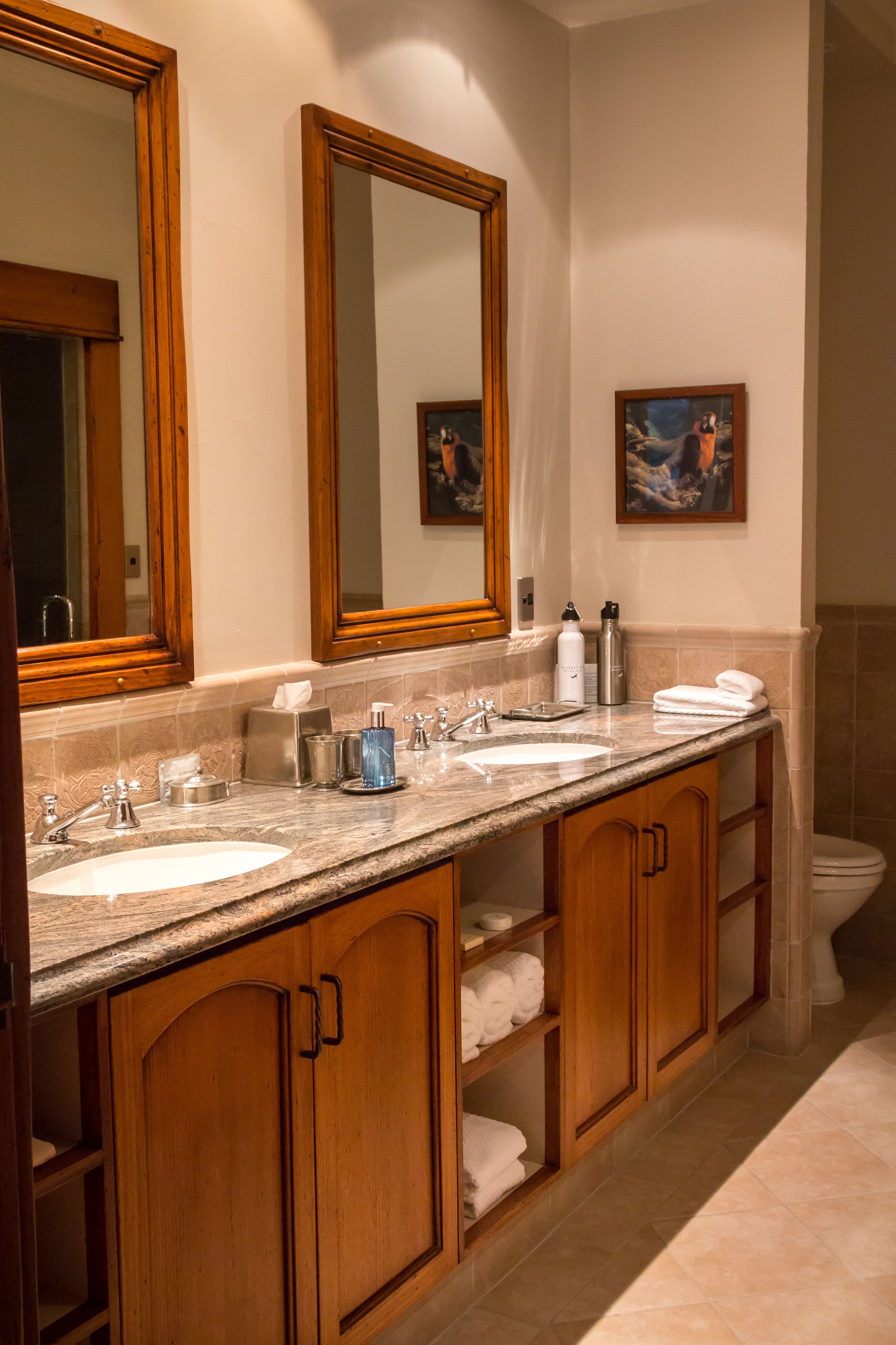 A bathroom with two sinks, wooden cabinets, a large mirror, and a painting on the wall.
