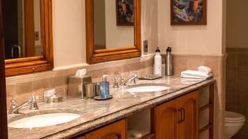 A bathroom with two sinks, wooden cabinets, a large mirror, and a painting on the wall.