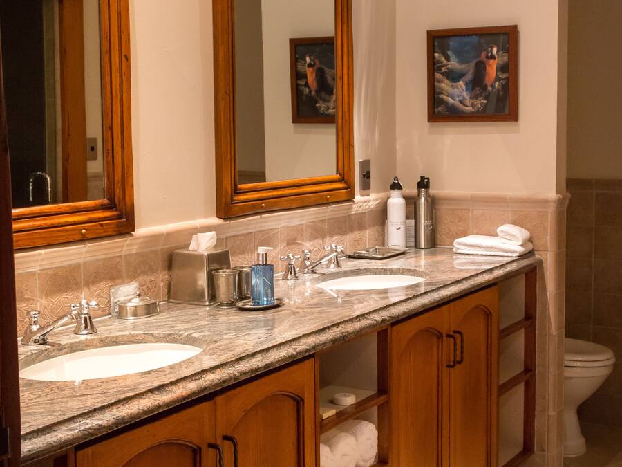 A bathroom with two sinks, wooden cabinets, a large mirror, and a painting on the wall.
