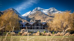 A mountain lodge with a stone facade, large windows, and a view of snow-capped mountains. - Blanket Bay (Glenorchy)