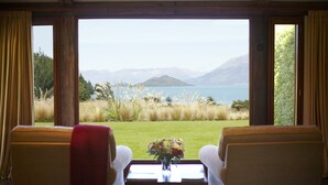 A room with a view of a lake and mountains, featuring two chairs and a table with a vase of flowers. - Blanket Bay (Glenorchy)