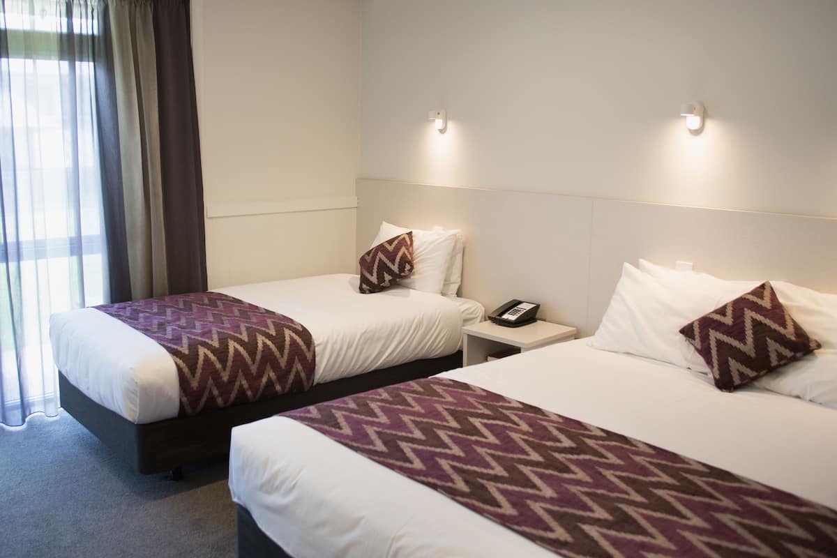 A hotel room with two beds, each with a patterned throw blanket, a bedside table with a phone, and a wall-mounted light fixture.