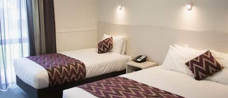 A hotel room with two beds, each with a patterned throw blanket, a bedside table with a phone, and a wall-mounted light fixture.