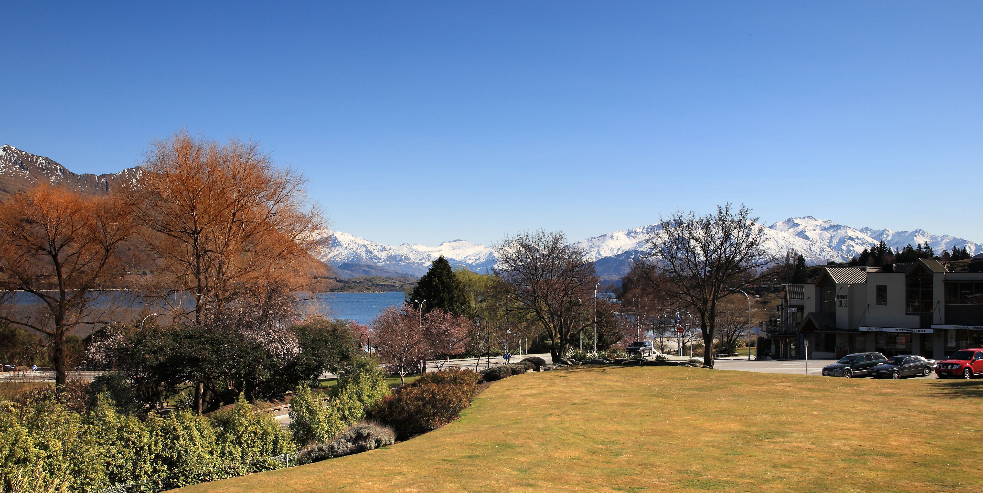 A view of a lake with mountains in the background, surrounded by trees and buildings.