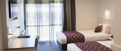 A hotel room with two beds, a desk, a chair, a TV, and a window with curtains.