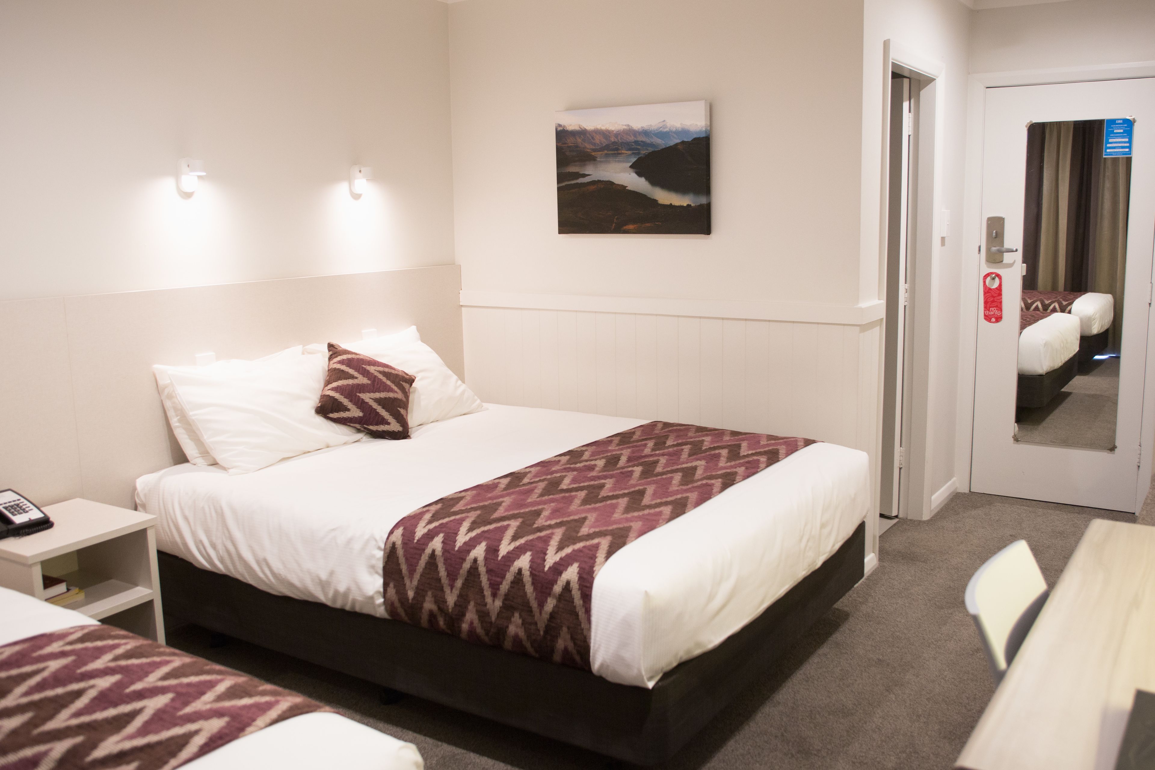 A hotel room with a bed, bedside table, and a painting on the wall.