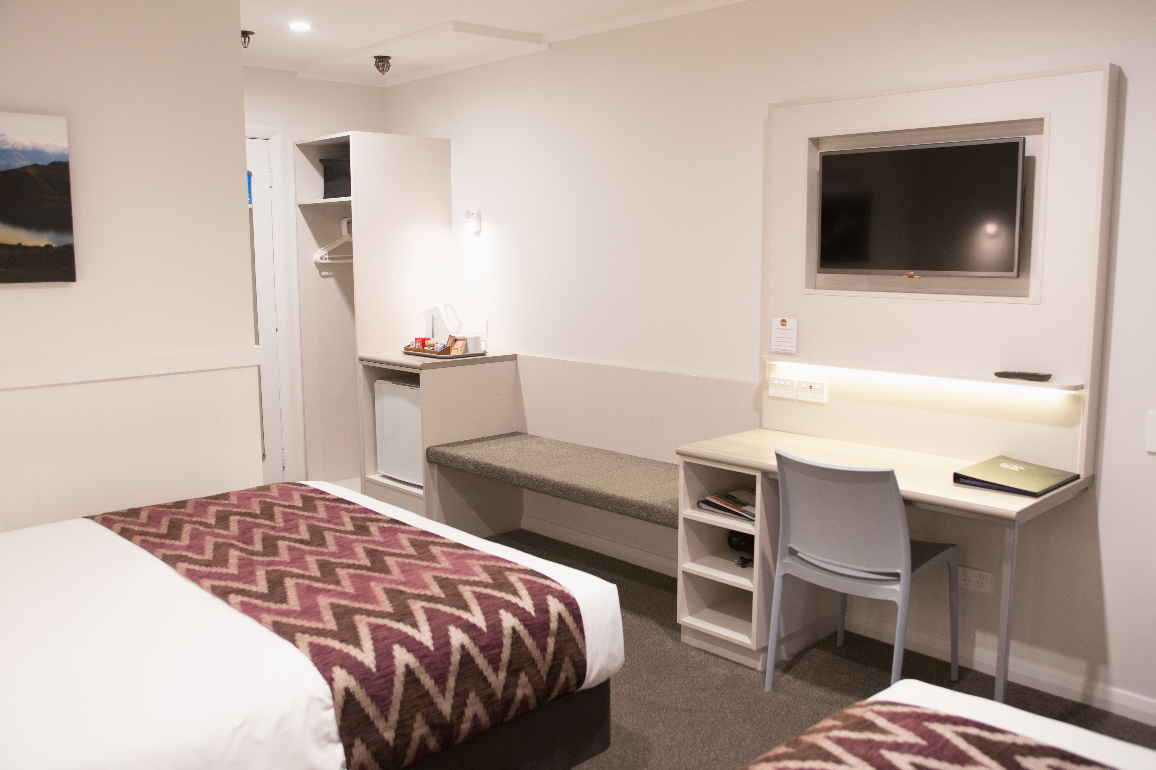 Habitación de hotel con cama, escritorio con silla, televisor y un pequeño rincón de descanso.